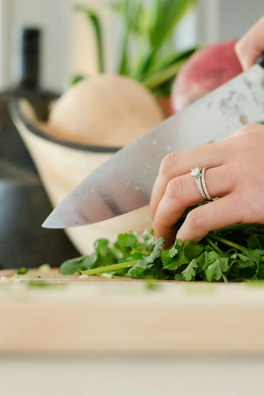 Hands chopping fresh coriander on a wooden board with a chef's knife