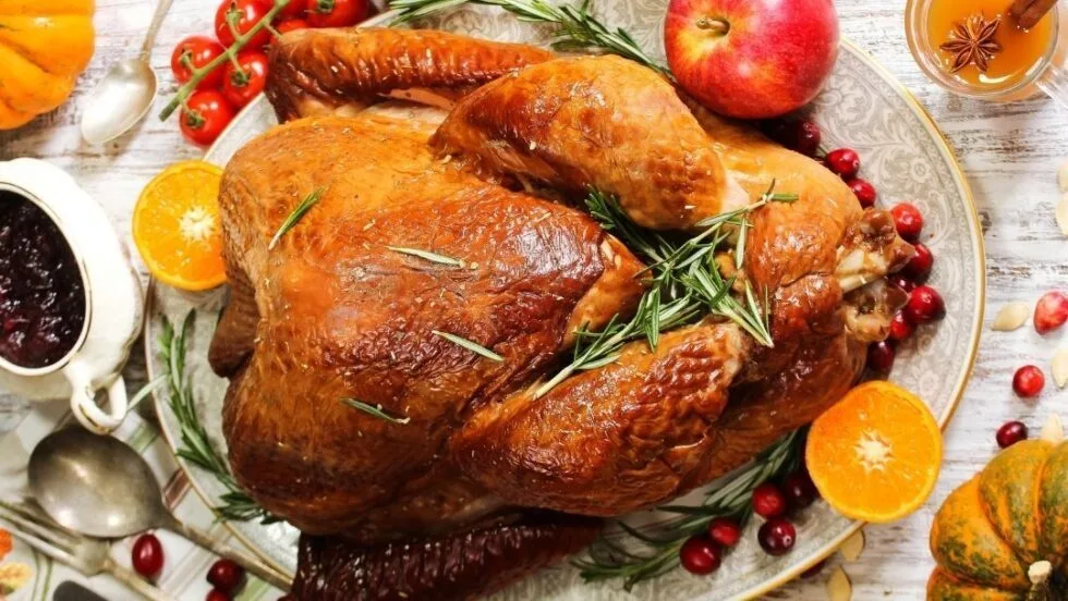 Roast turkey on a platter with rosemary, cranberries, orange halves and a bowl of cranberry sauce